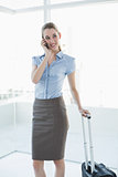Cheerful lovely businesswoman phoning while standing next to her case