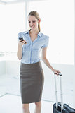 Beautiful content businesswoman using her smartphone standing in her office