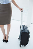 Mid section on slender classy businesswoman holding a suitcase
