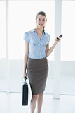 Calm content businesswoman holding her smartphone and briefcase