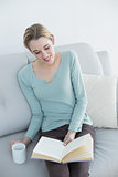 Cheerful casual woman reading a book holding a cup