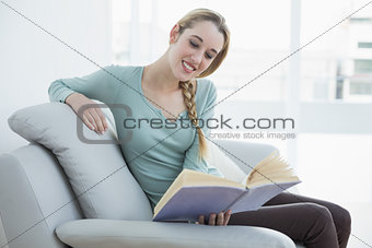 Young casual woman reading a book while sitting smiling on couch