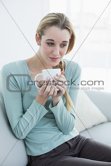 Gorgeous relaxing woman sitting on couch holding a cup