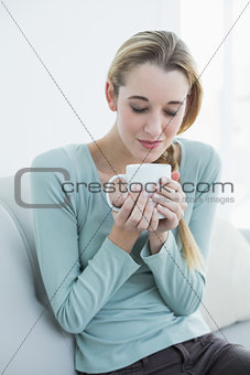 Gorgeous casual woman holding joyfully a cup sitting on couch