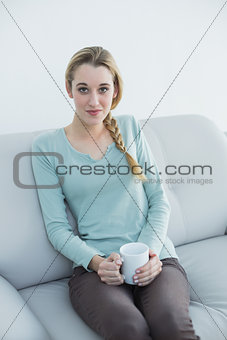 Natural young woman holding a cup sitting on couch