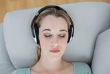 Lovely natural woman listening with headphones to music lying on a couch