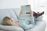 Slim casual woman reading newspaper lying on couch