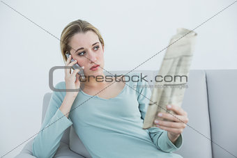 Casual thinking woman phoning while sitting on couch