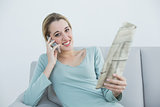 Calm woman phoning while holding newspaper and sitting on couch