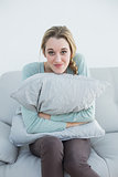 Lovely sweet woman sitting on couch cuddling with a pillow