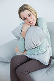 Gorgeous smiling woman cuddling with pillow sitting on couch