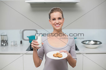 Happy gorgeous model looking at camera holding glass of milk and cookies