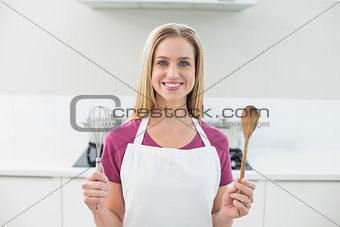 Casual smiling blonde showing wooden spoon and whisk