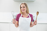 Casual cheerful blonde showing wooden spoon and whisk