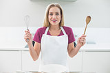 Casual laughing blonde showing wooden spoon and whisk