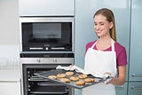 Casual smiling woman holding baking tray with cookies