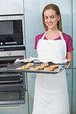 Casual cheerful woman holding baking tray with cookies