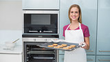 Casual gleeful woman holding baking tray with cookies