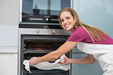 Casual smiling woman putting baking tray in oven