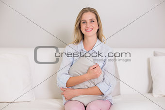 Casual smiling blonde sitting on couch holding pillow