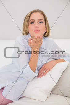 Happy casual blonde relaxing on couch blowing kiss