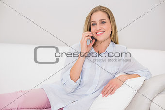 Happy casual blonde relaxing on couch phoning
