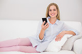 Happy casual blonde relaxing on couch holding smartphone