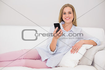Happy casual blonde relaxing on couch holding smartphone