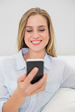 Laughing casual blonde relaxing on couch holding smartphone