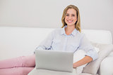 Smiling casual blonde relaxing on couch using laptop