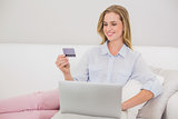 Smiling casual blonde relaxing on couch doing online shopping
