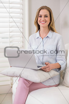 Cheerful casual blonde sitting on couch using laptop
