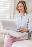 Happy casual blonde sitting on couch using laptop