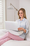 Laughing casual blonde sitting on couch using laptop