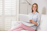 Gleeful casual blonde sitting on couch using laptop