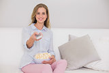 Happy casual blonde sitting on couch holding remote