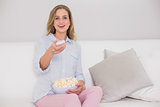Laughing casual blonde sitting on couch holding remote