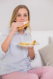 Happy casual blonde sitting on couch eating sandwich