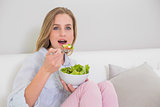Surprised casual blonde sitting on couch eating salad