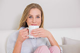 Content casual blonde sitting on couch holding mug