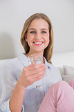 Happy casual blonde sitting on couch holding glass of water