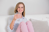 Smiling casual blonde sitting on couch holding glass of water