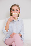 Content casual blonde sitting on couch drinking from disposable cup