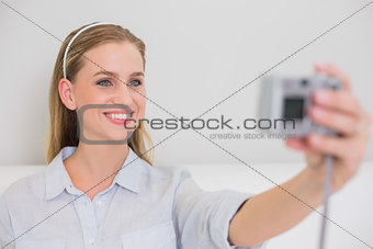 Smiling casual blonde sitting on couch taking a picture of herself