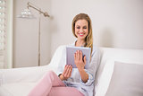 Smiling casual blonde sitting on couch using tablet
