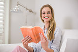 Cheerful casual blonde sitting on couch holding a book