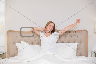 Natural happy woman yawning and sitting in bed