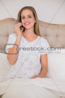 Natural smiling woman phoning and sitting in bed