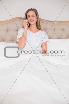 Natural cheerful woman phoning and sitting in bed