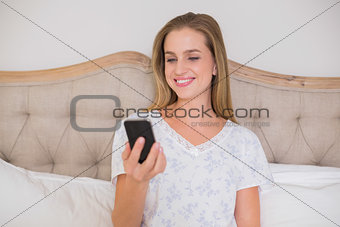 Natural happy woman sitting in bed looking at smartphone